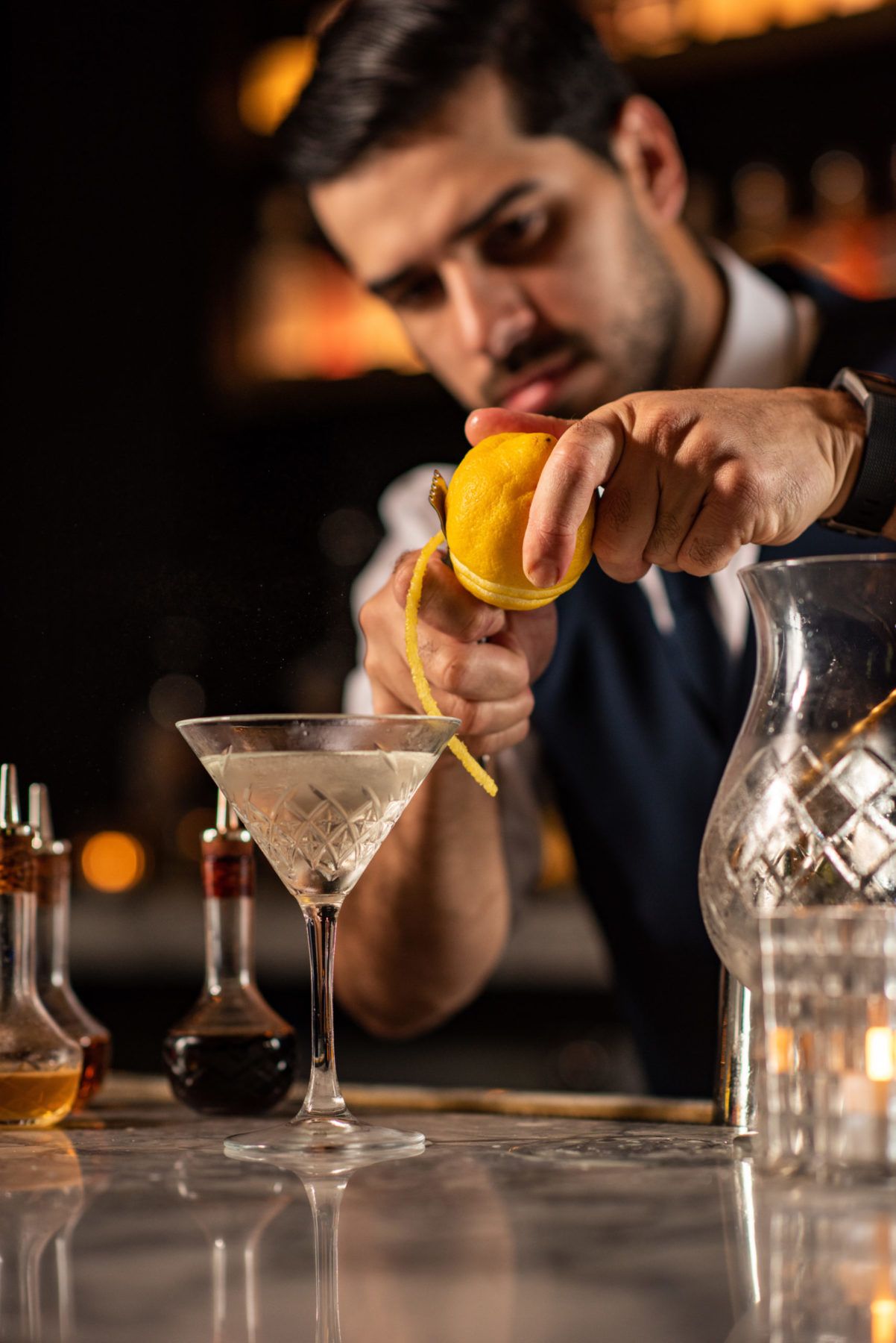 Bartender peeling lemon over a martini glass at bar
